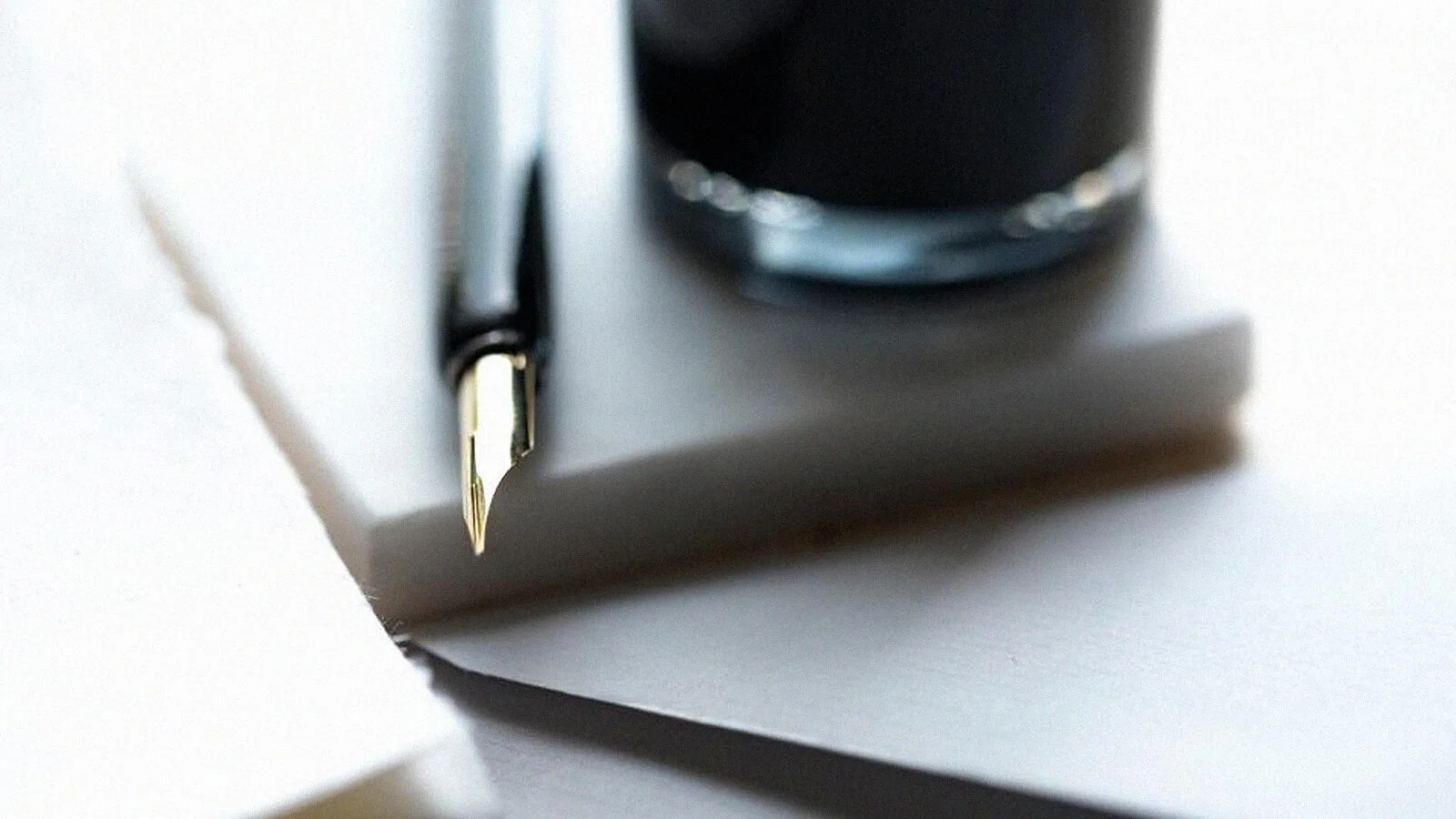 A fountain pen and ink bottle beside a folded sheet of paper.