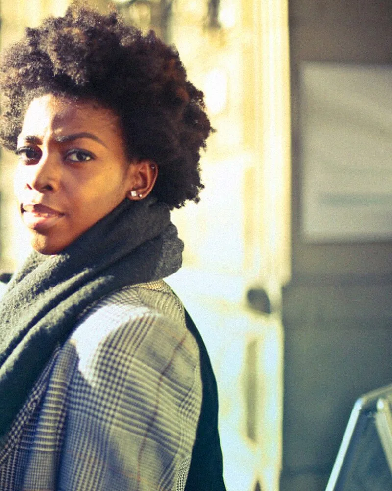 A woman in a checked coat and green scarf on a city street.