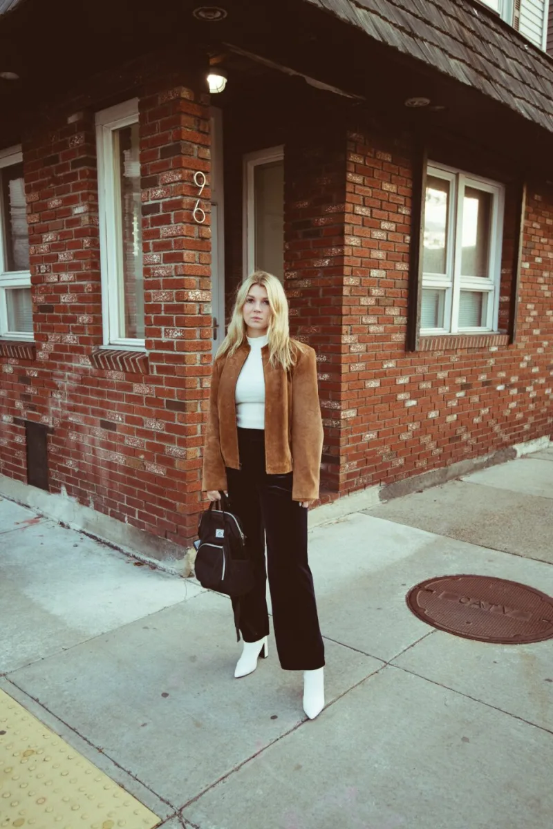 A woman in a camel jacket and wide trousers on a brick-lined street.