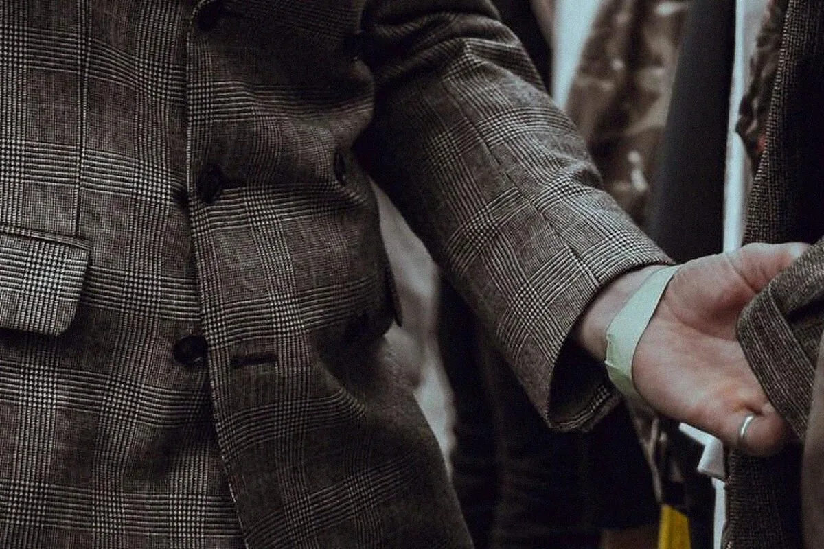 Detail of a glen-check suit sleeve, a hand reaching for a jacket on a clothing rail.